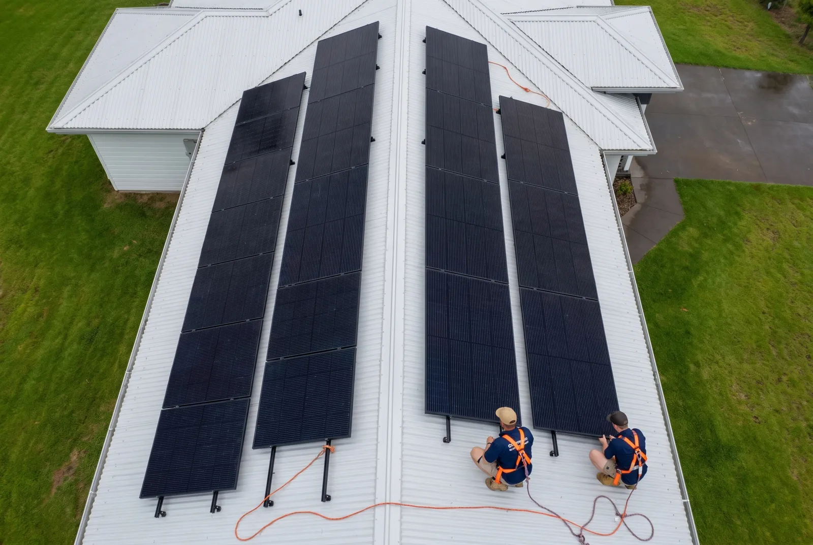 Two installers fitting a row of solar panels on a metal roof, seen from above
